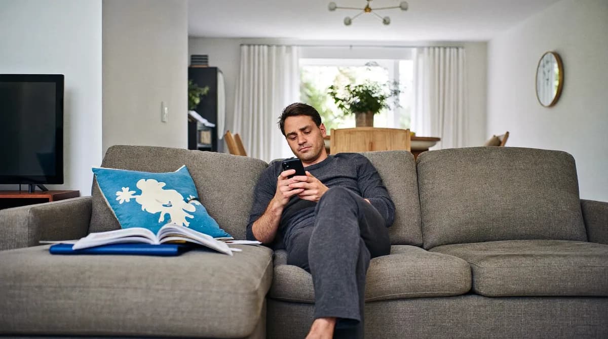 Mann wechselt entspannt per Smartphone auf dem Sofa den Stromanbieter